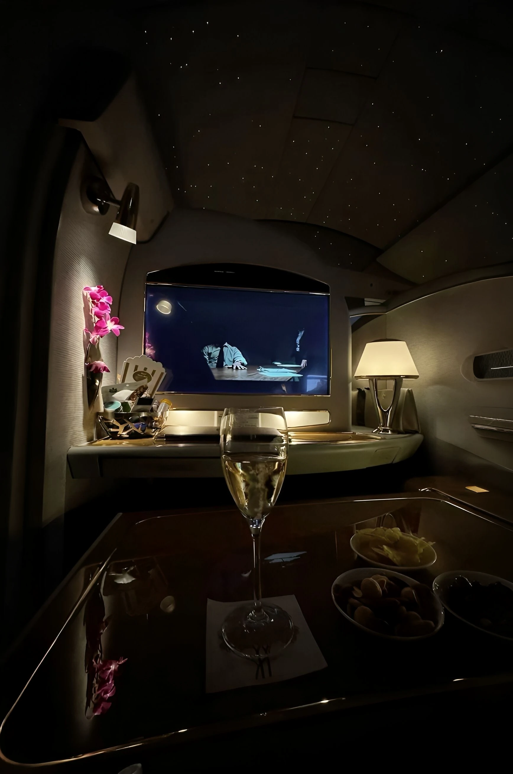Champagne on a polished suite table at night, a film playing under the starlit ceiling