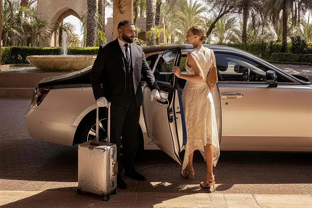 A white-gloved chauffeur opening the car door for a guest at a palm-lined resort