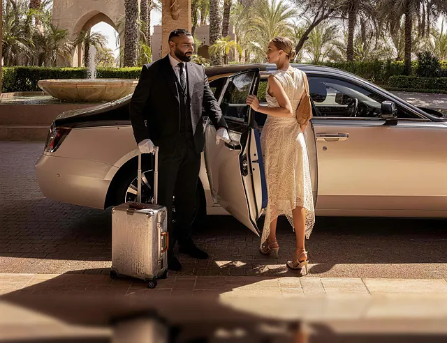 A white-gloved chauffeur opening the car door for a guest at a palm-lined resort