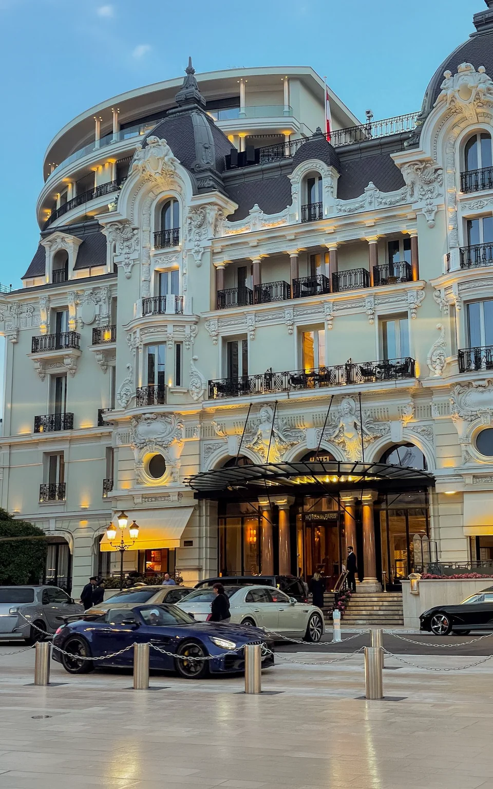 A grand hotel facade lit at dusk, cars waiting under the entrance canopy