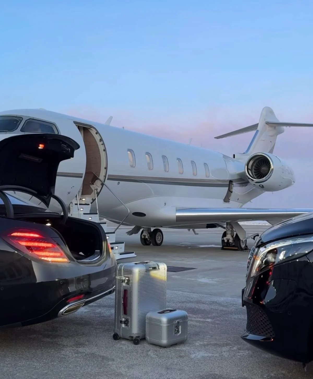 A white private jet at dusk on the tarmac, chauffeur cars and luggage alongside